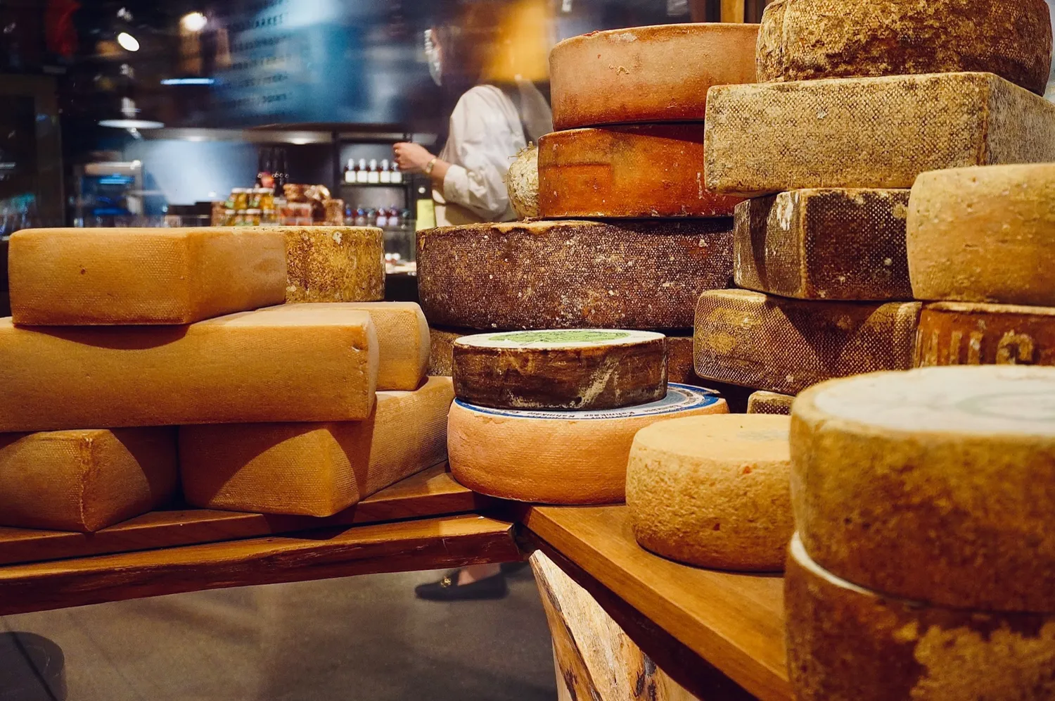 Wheels of artisanal cheese stacked on wooden shelves — the local, seasonal sourcing behind Rosmarino, Indiranagar