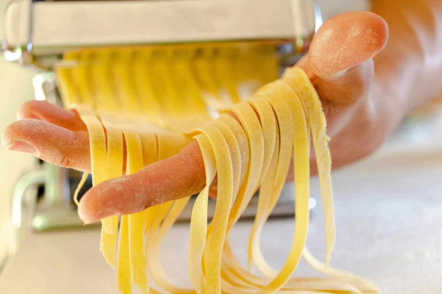Fresh pasta being cut into ribbons through a hand-cranked pasta machine at Rosmarino, Indiranagar