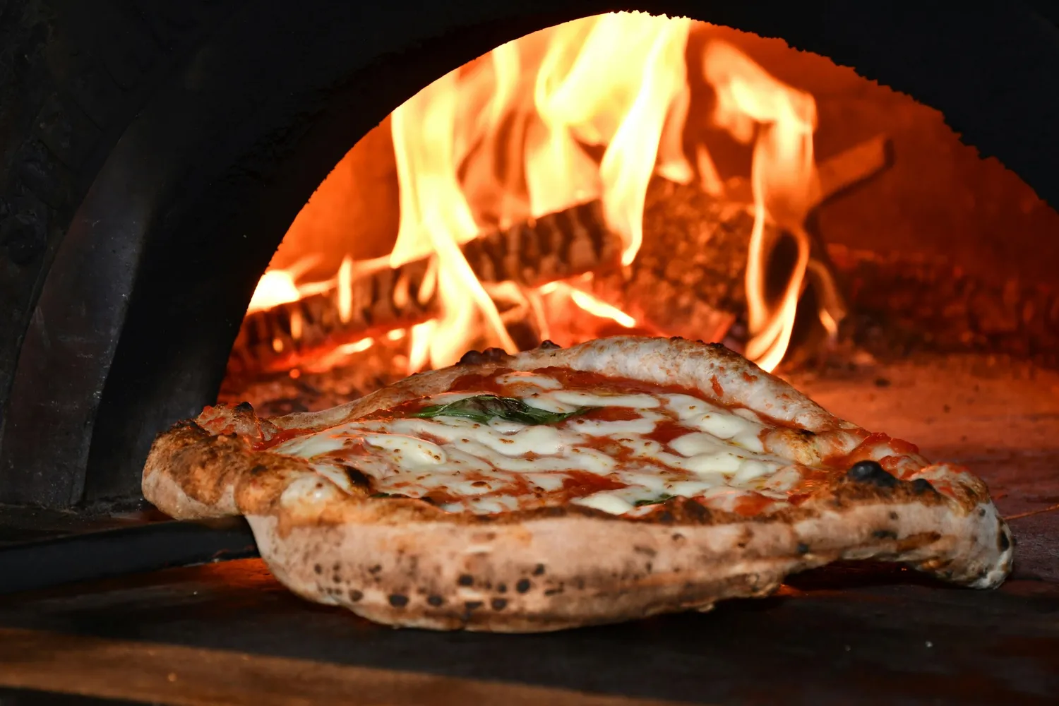 A Neapolitan pizza blistering in the wood-fired oven with live flames behind, at Rosmarino, Indiranagar