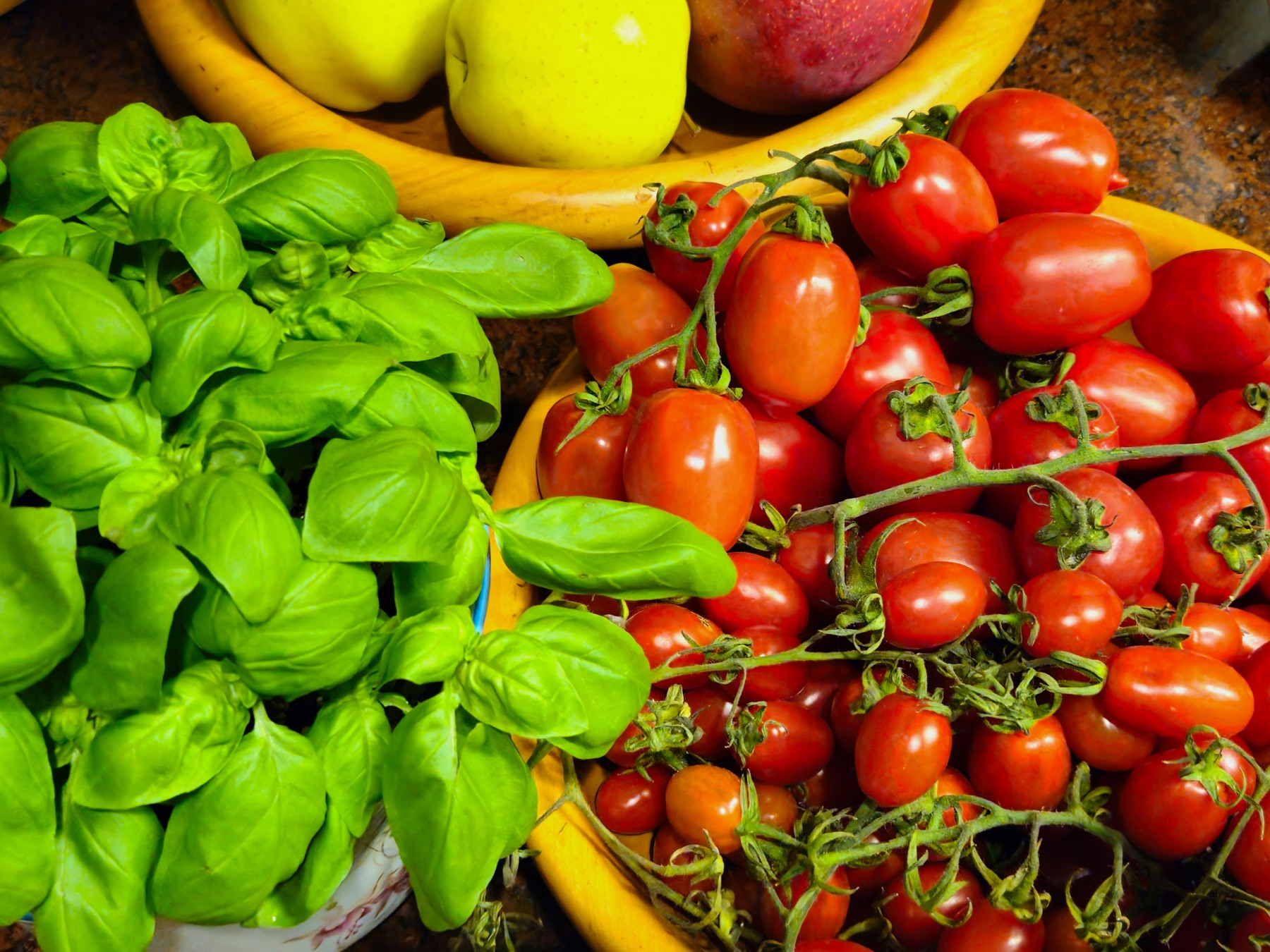 Fresh basil and vine-ripened tomatoes with seasonal fruit in rustic bowls
