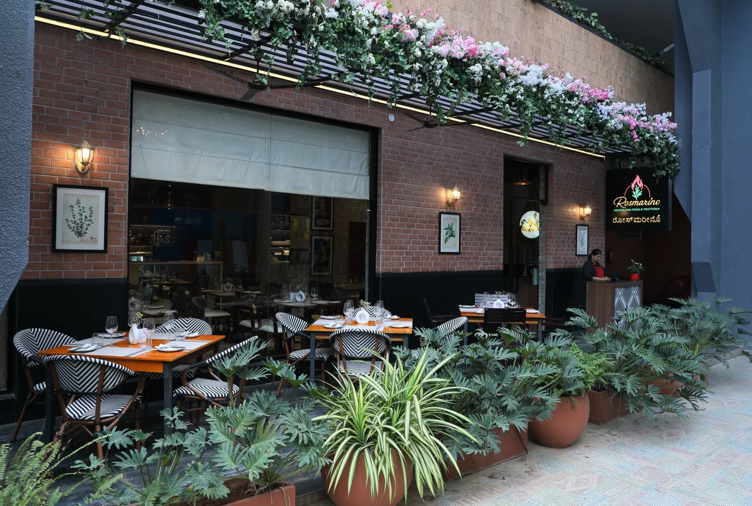 Rosmarino's alfresco terrace, Indiranagar — bistro chairs, greenery and a flowering pergola at the entrance