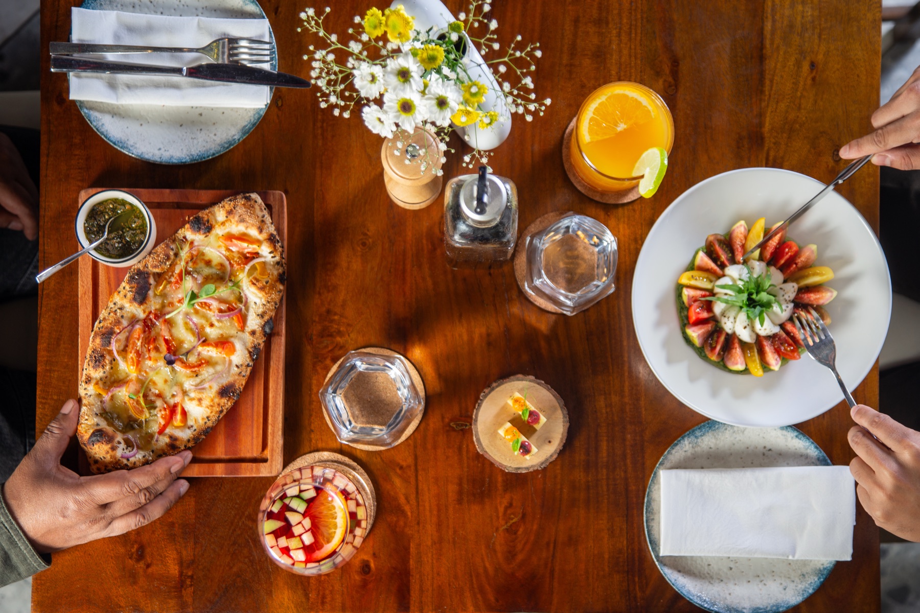 Overhead table spread at Rosmarino, Indiranagar — wood-fired flatbread, fig and bocconcini salad, sangria and cocktails