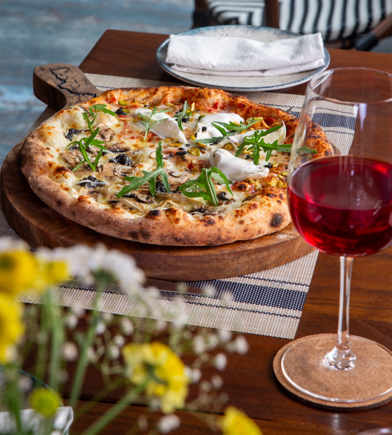 A wood-fired half-and-half pizza with burrata and rocket, served with a glass of red at Rosmarino, Indiranagar